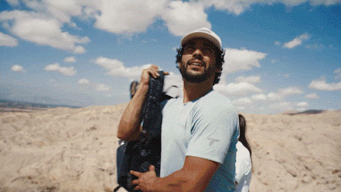 A gif of a man climbing up rocks to get to the top in an arid environment.