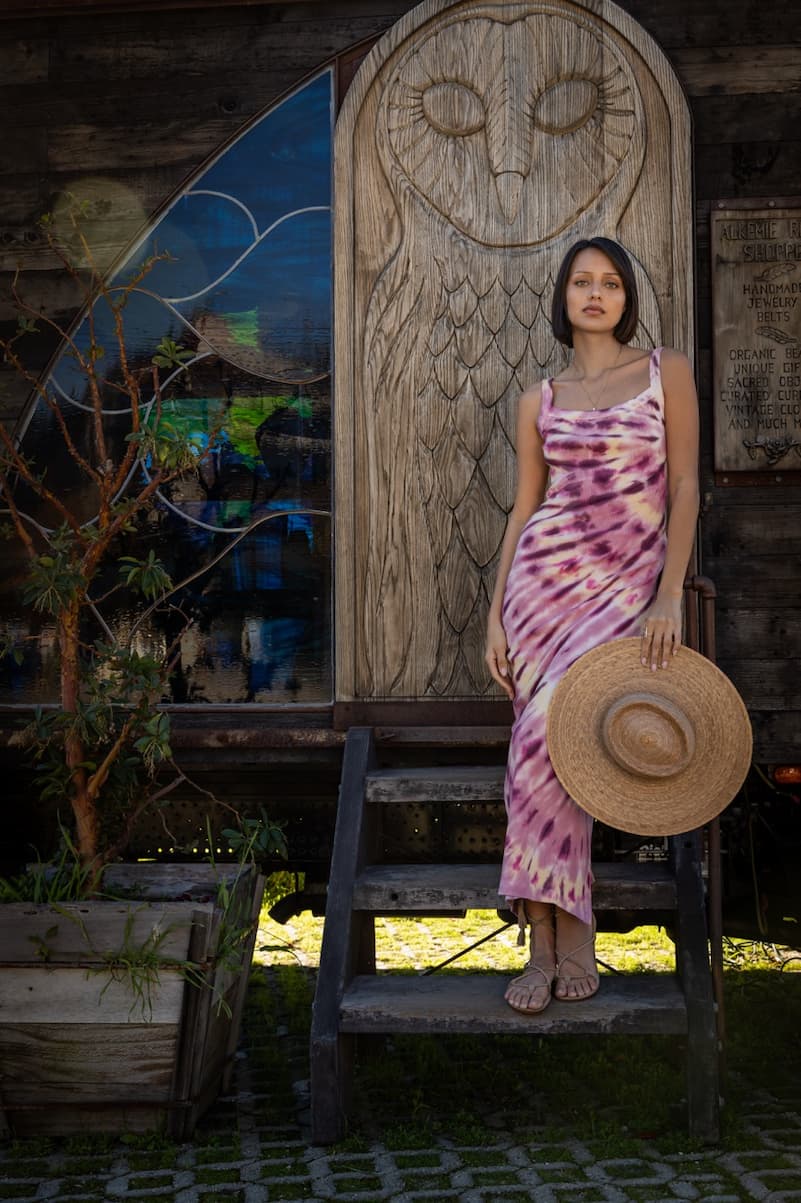 Woman wearing a Pink tie-dye dress standing outside in front of a wooden door