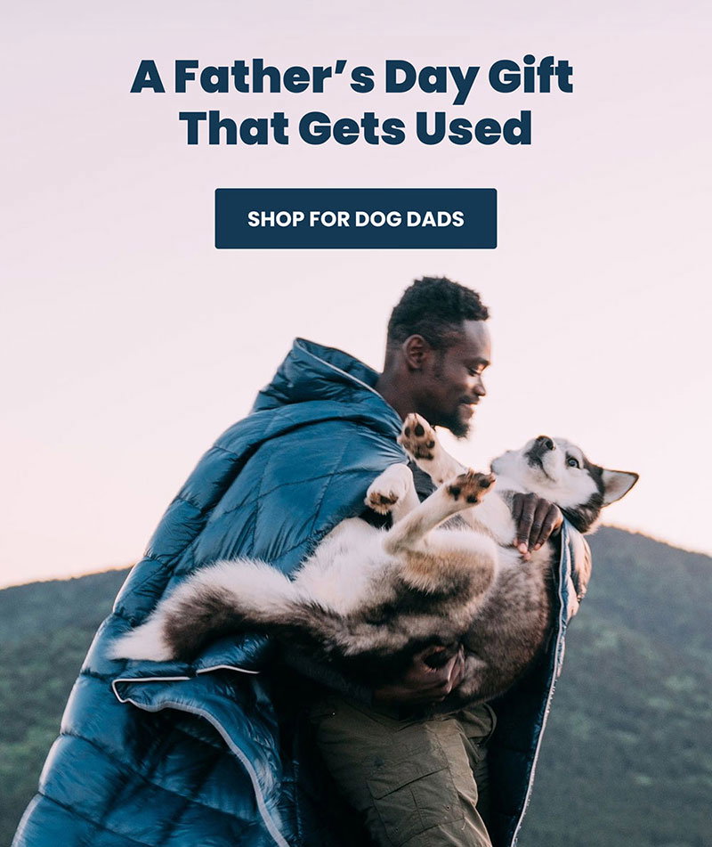 Dad carries a husky breed dog in his arms while wearing a Rumpl blanket