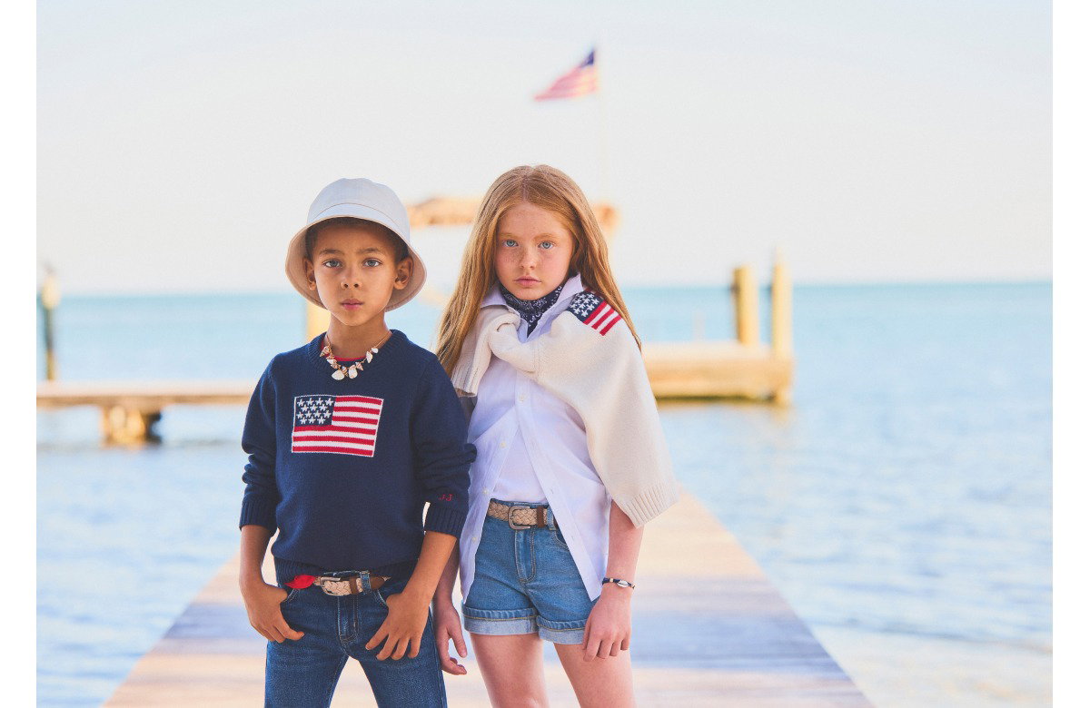 Two children wearing American flag apparel standing by water with wooden dock in background