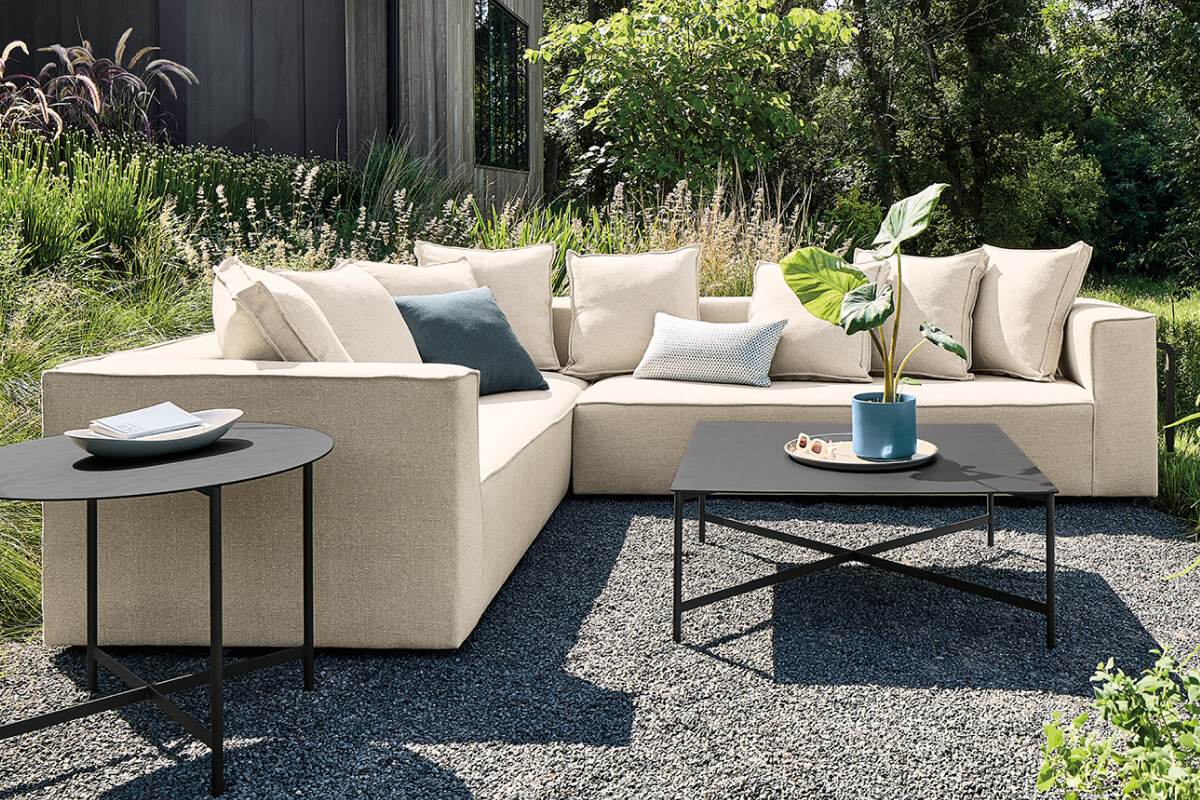 Oasis sectional with neutral cushions and black Circuit tables styled on a landscaped outdoor patio.