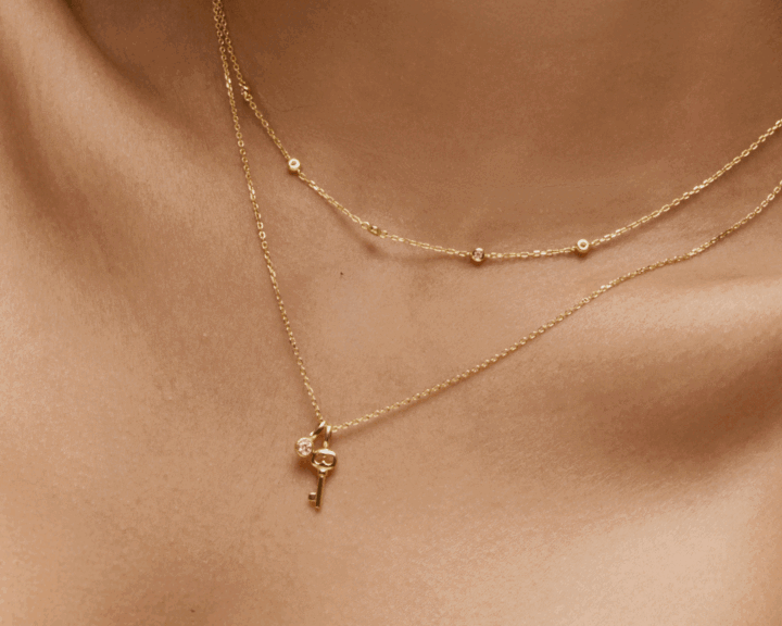 Close-up of layered yellow gold necklaces with key charm pendant and bezel-set diamond accents on neckline.