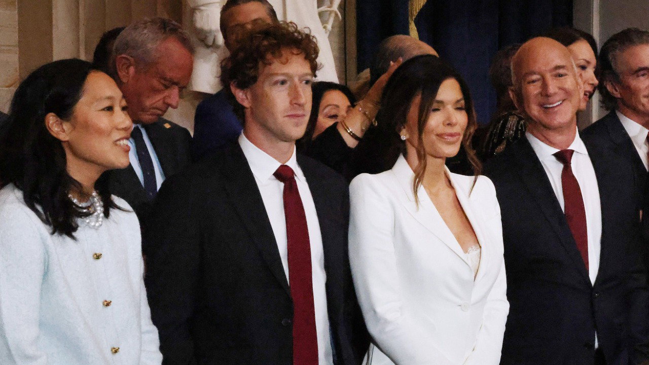Priscilla Chan and Mark Zuckerberg are stood in a row on the left beside Lauren Bezos, Jeff Bezos, Sundar Pichai and Elon Musk. They all wear formalwear, and Chan and Lauren Bezos wear white outfits. There are a row of empty chairs in front of them.