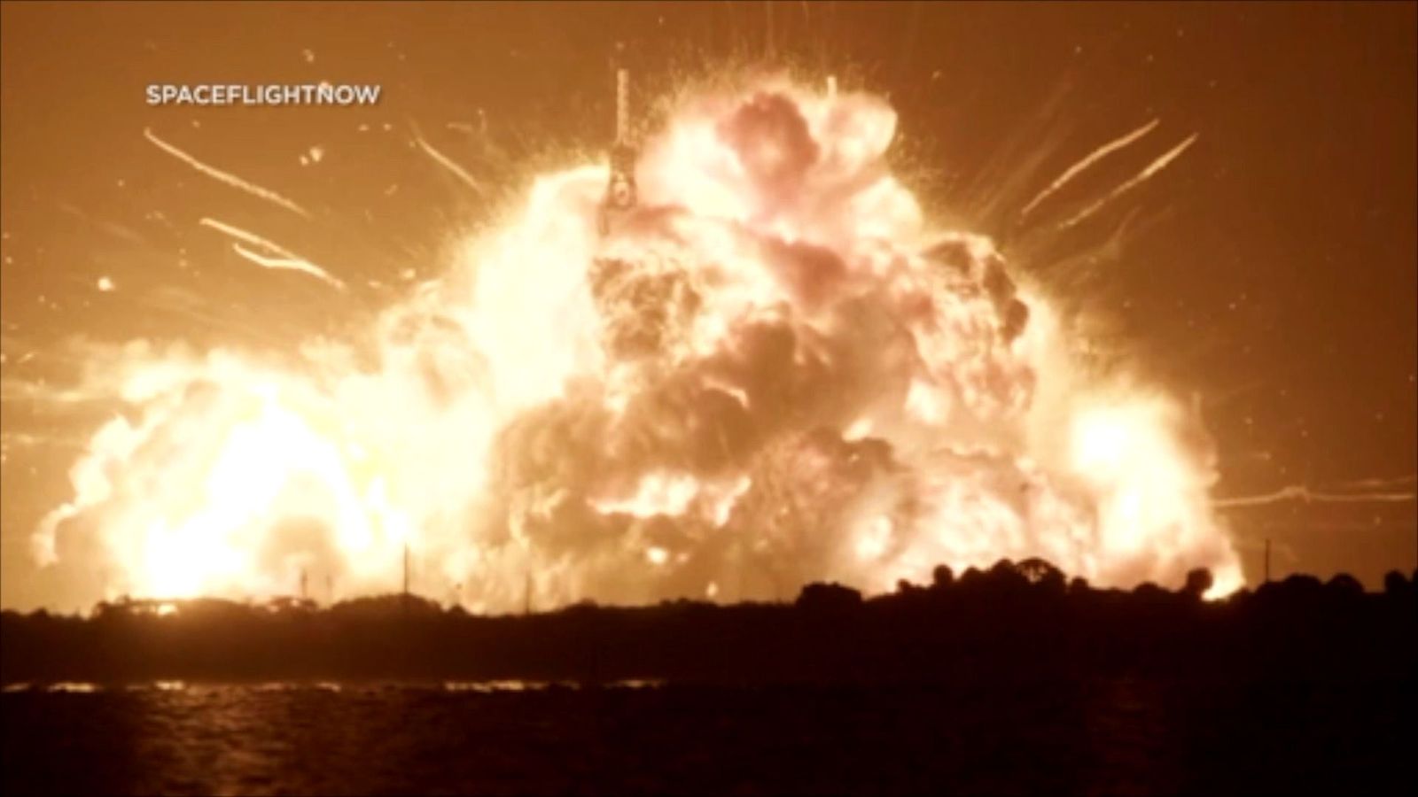 A huge fireball is seen lighting up the dark sky. Sparks are seen flying away from it and trees are silhouetted in front of it.