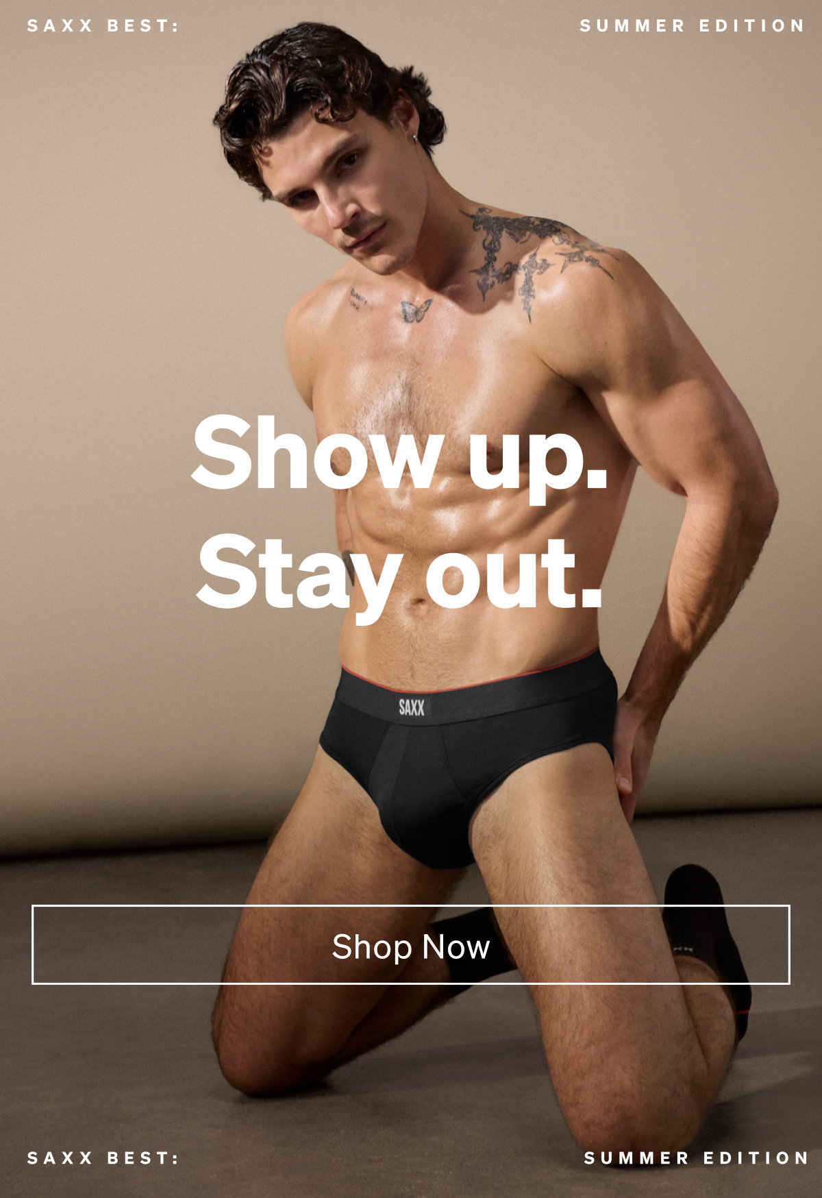 Model kneeling indoors wearing black SAXX briefs with “Show up. Stay out.” text and Shop Now CTA.