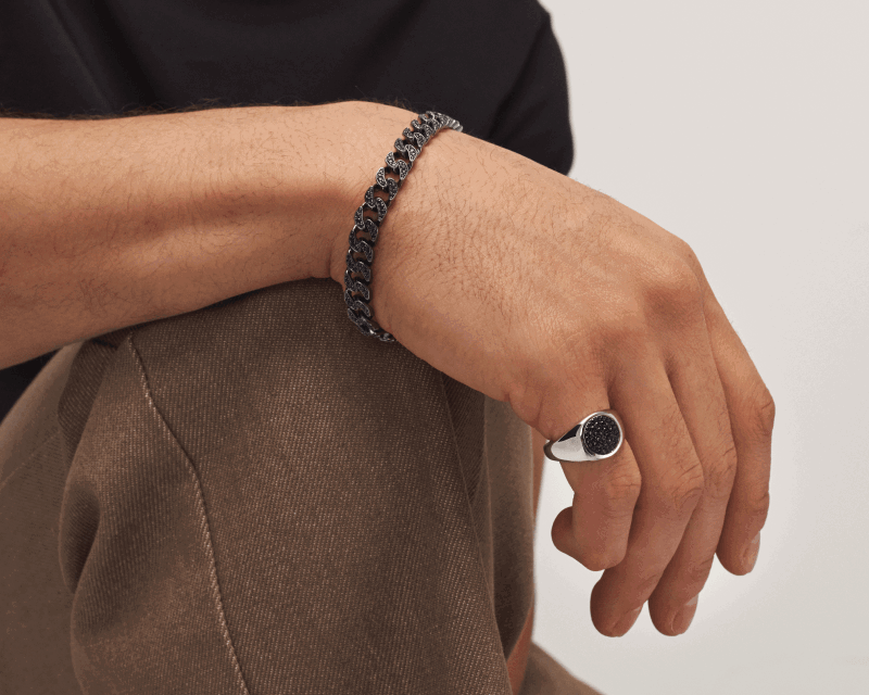 Black chain bracelet and silver signet ring with black textured face, shown worn on hand.