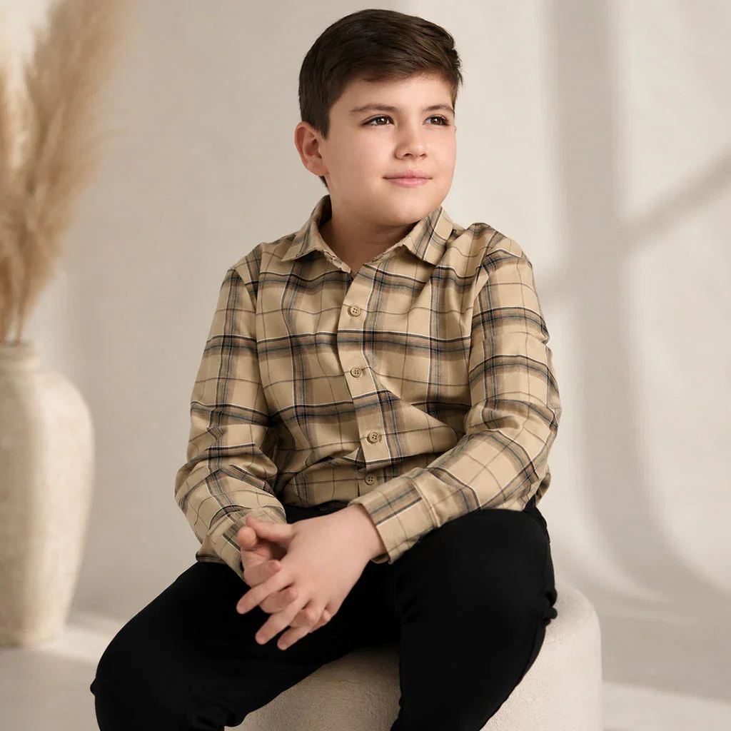 Young boy wearing a tan plaid button-up shirt and black pants, seated against a neutral background for Mofi Clothing.