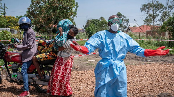 A health worker gestures for help with a patient as they are lifted from the back of a motorcycle.