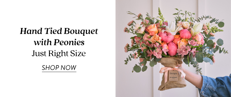 Product feature for the Hand Tied Bouquet with Peonies in Just Right Size, showing the bouquet being held out by someone in a blue sleeve. The bouquet includes pink, coral, peach, and green flowers wrapped in burlap. Text on the left reads “Hand Tied Bouquet with Peonies, Just Right Size” with a “Shop Now” link.