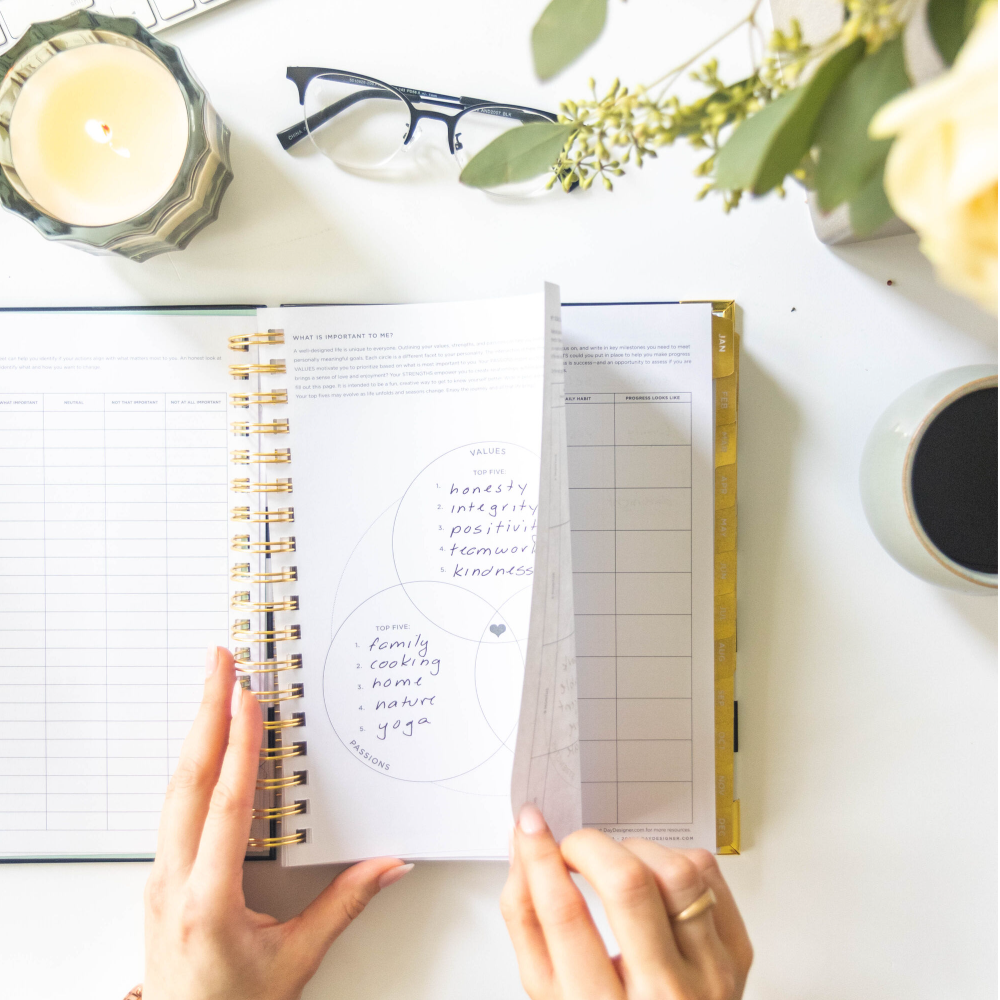 hands holding open book day designer planner, showing goal-setting written on page, coffee, white background