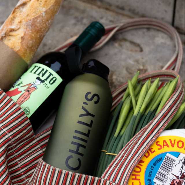 A striped bag containing a baguette, a wine bottle, a green Chilly's bottle, and green onions.