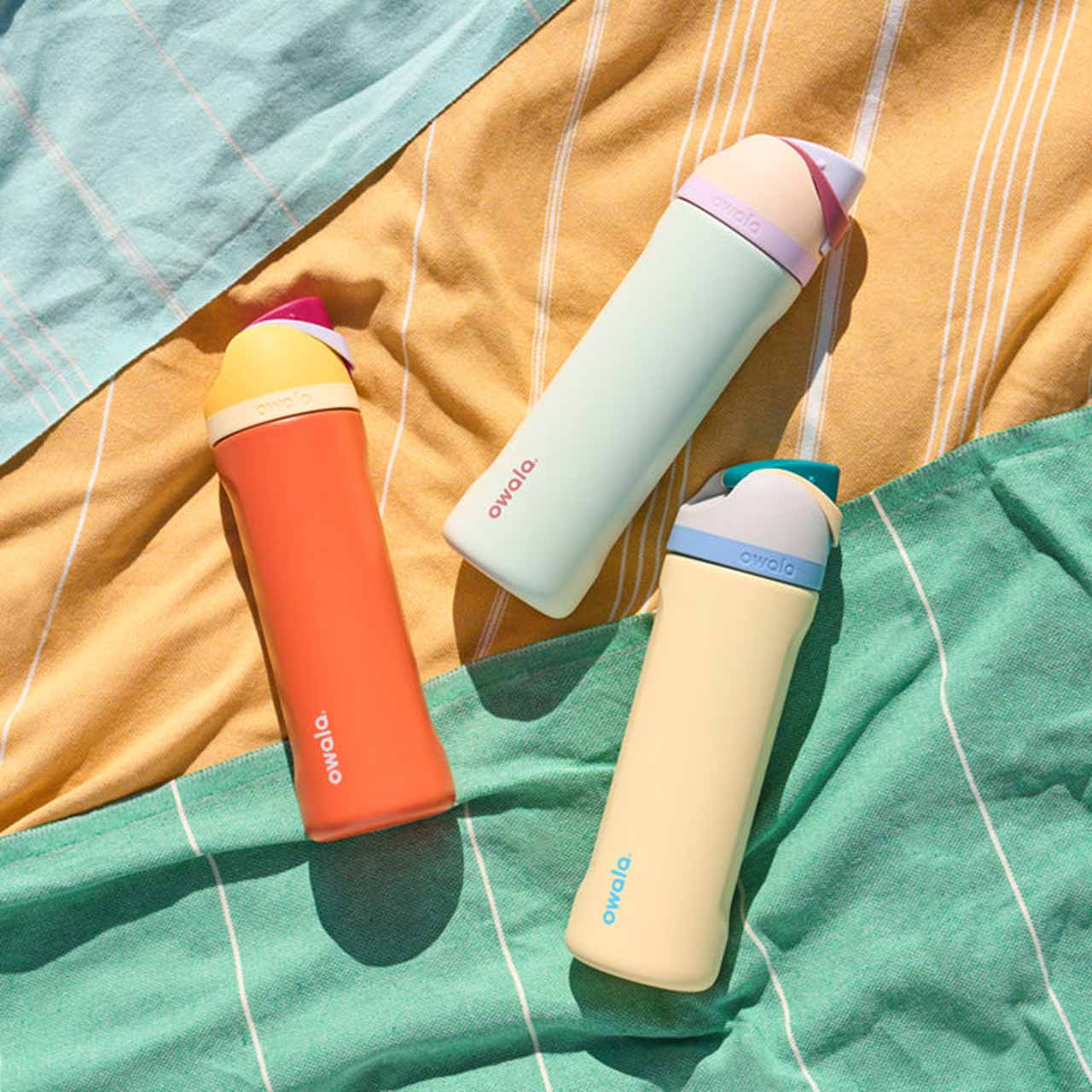 Three colorful thermos bottles on a striped blanket.