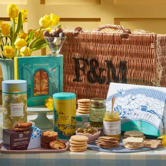 A wicker hamper labeled 'F&M' surrounded by assorted biscuits, jars, colorful tins, and a bouquet of yellow tulips.
