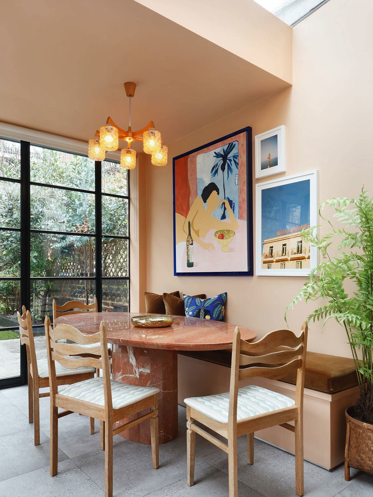 A bright dining nook with a marble table, wooden chairs, and colourful artwork on peach walls.