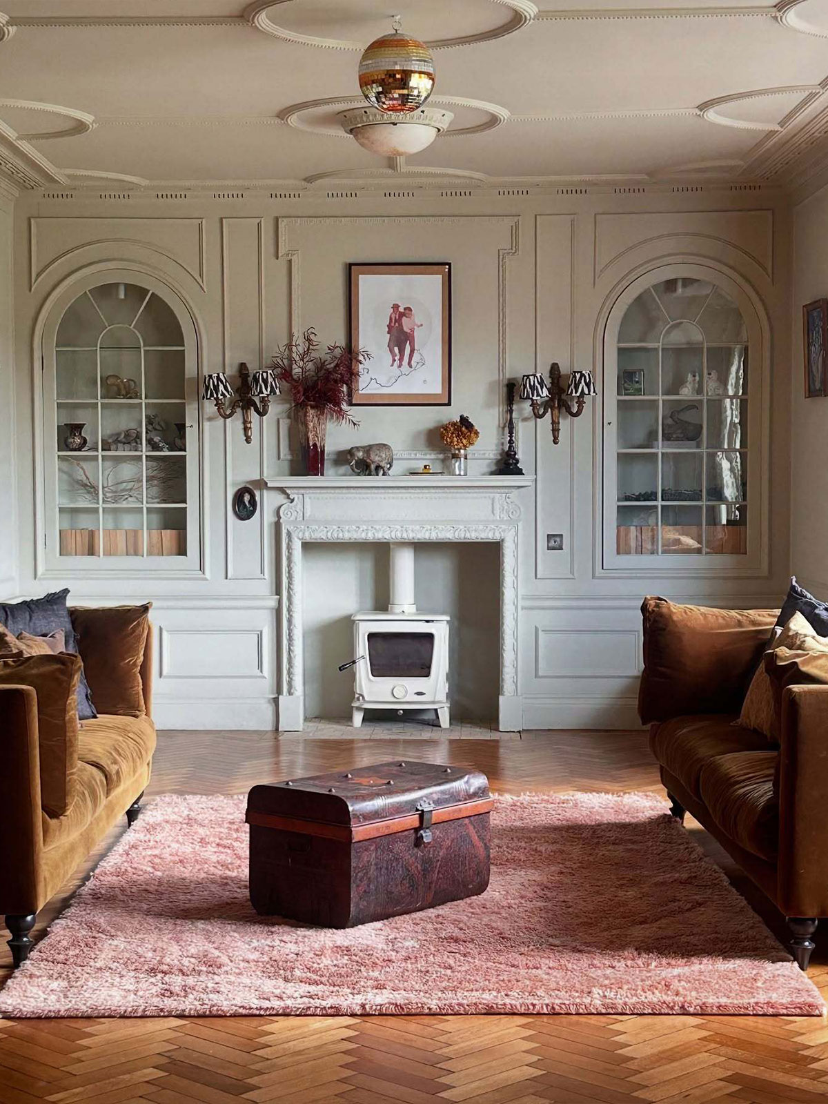 A traditional living room with brown sofas, a pink rug, and a white fireplace beneath a disco ball.