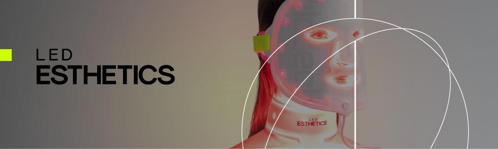 Dark background with a close-up product shot of a red LED face mask held by a person — hands only are visible.