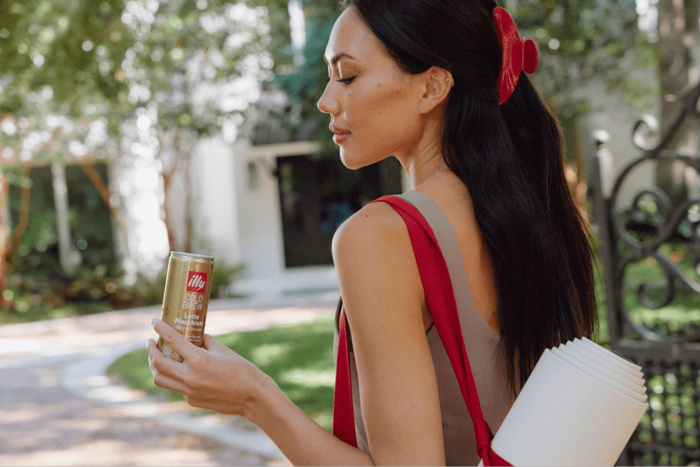 Woman holding a can of cold brew coffee while walking outdoors with a rolled yoga mat in her bag
