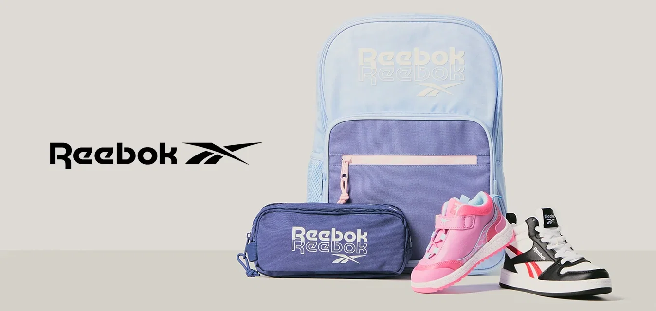 Hellblauer und lilafarbener Reebok-Rucksack, lilafarbenes Federmäppchen und zwei Kleinkind-Sneaker – ein pinker, ein schwarz-weißer – vor grauem Hintergrund.