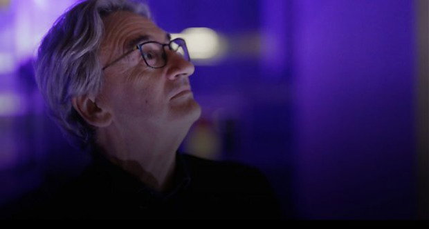 Fergal Keane wears glasses and looks upwards against a dim, purple-lit background.