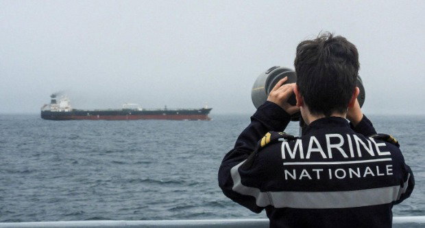 A French Navy officer wearing a black uniform labelled Marine Nationale observes an alleged Russian oil tanker sailing in the Atlantic ocean.