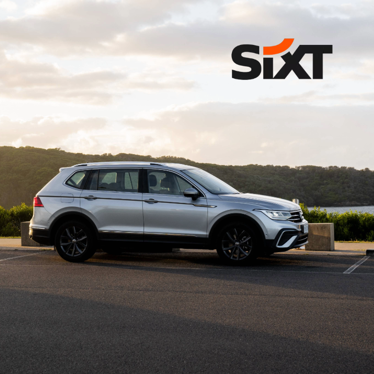 A silver car in front of a green landscape