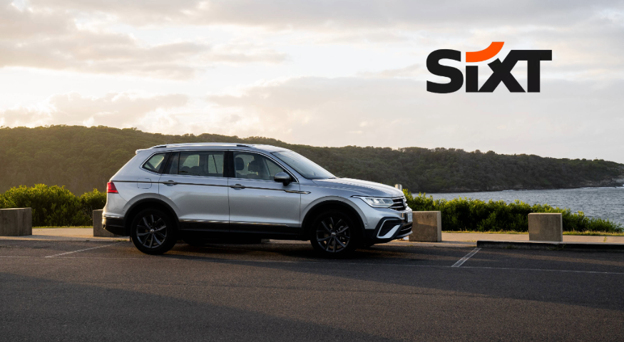 A silver car in front of a green landscape