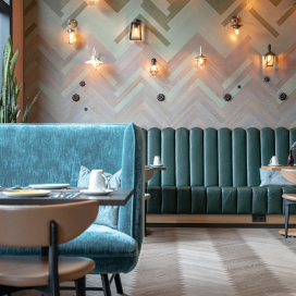 A lobby restaurant accented with turquoise featuring a large banquet and herringbone surfaces.