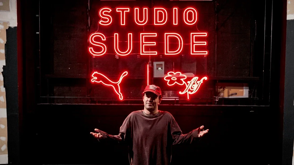 A medium shot shows a person wearing a red baseball cap and a dark long-sleeved shirt standing in front of a bright red neon sign that reads 'STUDIO S...