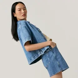 Giovane donna che si piega all'indietro indossando una giacca di jeans e una gonna con stivali da cowboy marroni su uno sfondo chiaro e uniforme.