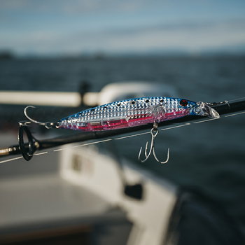 Close-up of a colourful hard-bodied fishing lure with treble hooks clipped to a rod on a boat with sea in background