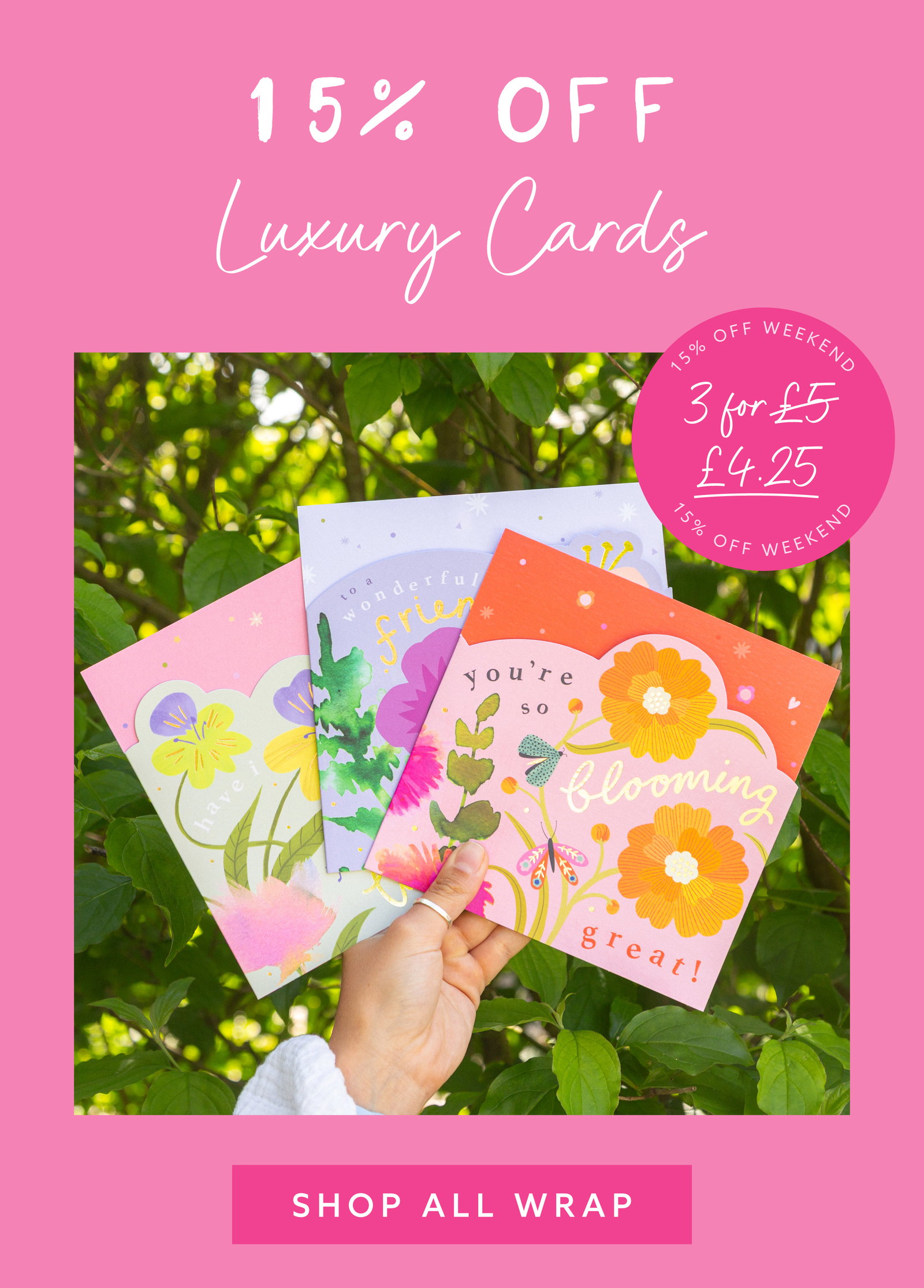 Pink promotional banner featuring luxury floral greeting cards held outdoors amongst leafy greenery with 15% off messaging and multibuy pricing details.