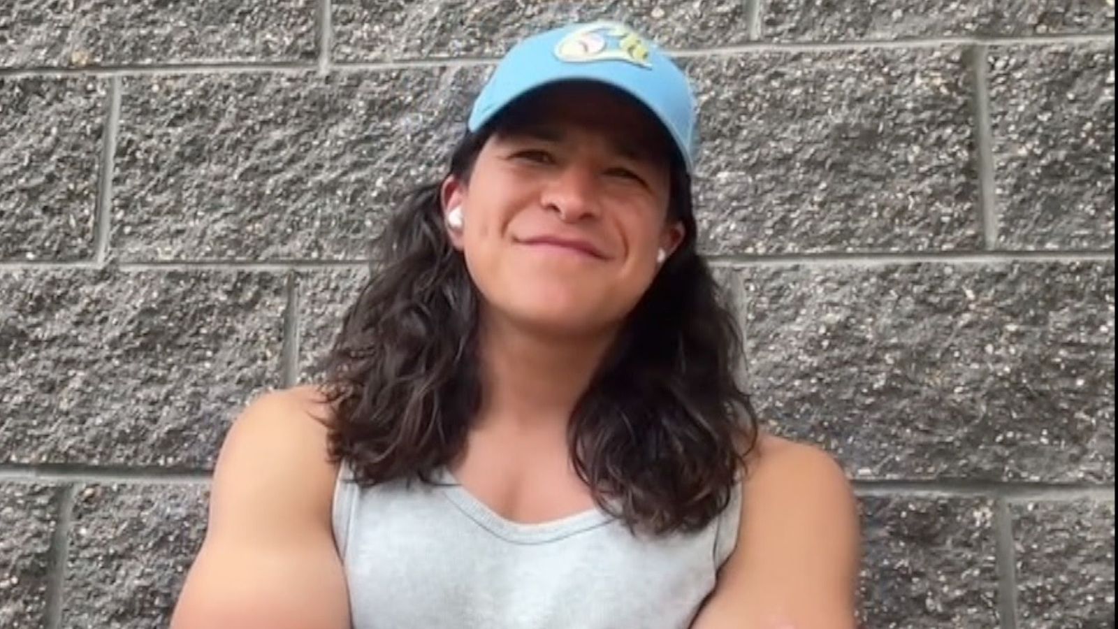 A screenshot of Cristo Fernández from an interview he gave to the BBC. He has shoulder-length, wavy dark brown hair and wears a blue cap and a grey vest.