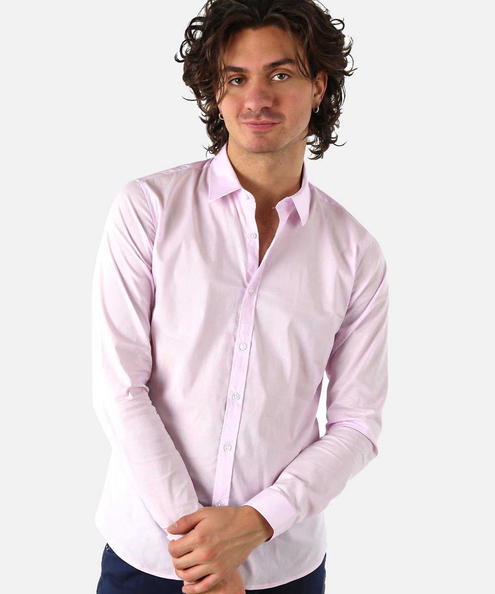Man wearing a light pink long-sleeved dress shirt against a plain white background, hands clasped and slight smile