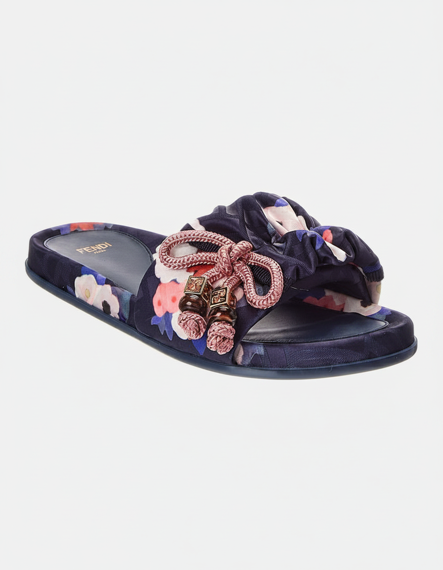 A navy blue slide sandal with a floral print and a decorative bow with tassels.