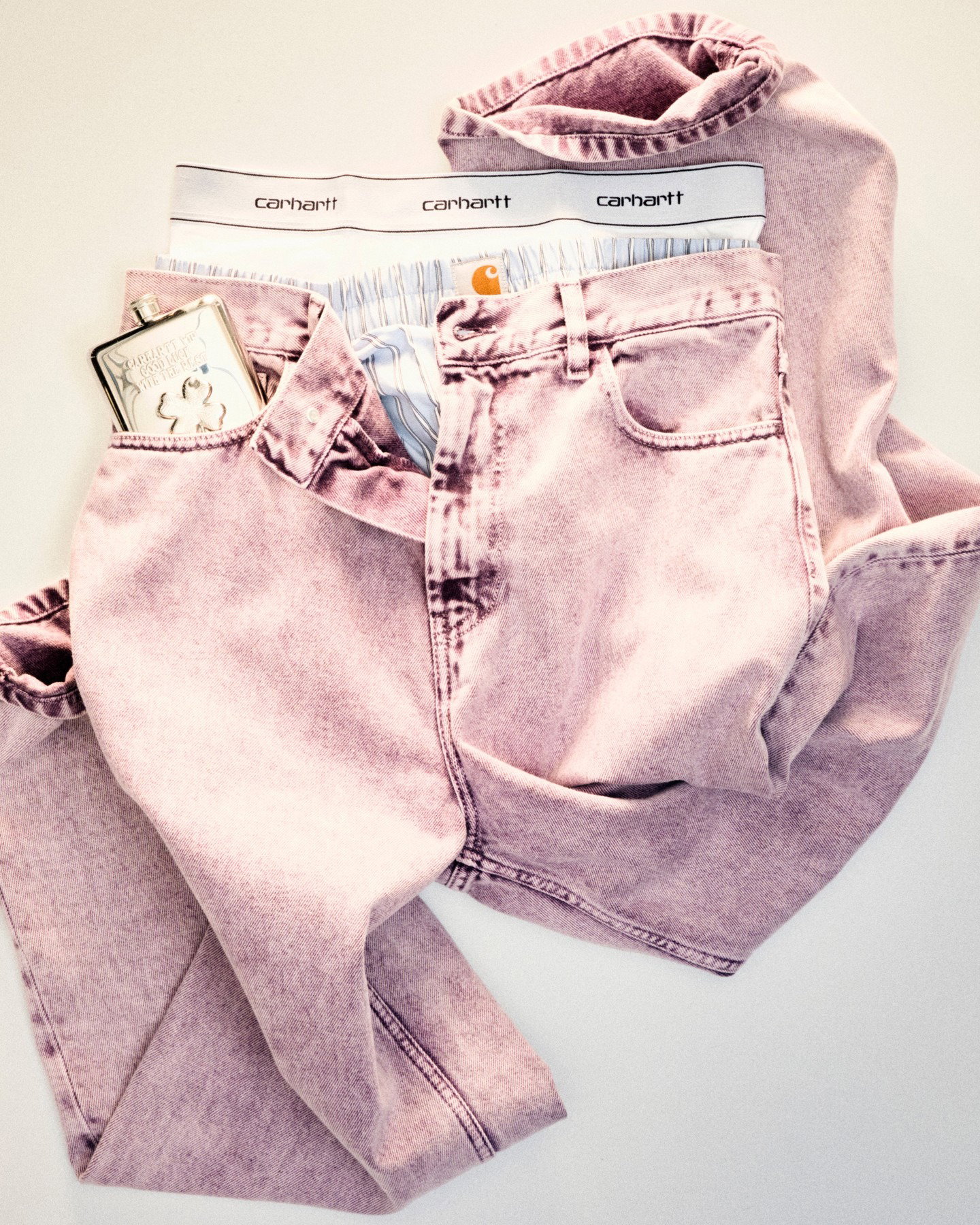 Pink washed jeans folded with Carhartt boxer waistband and a metal card case peeking from the front pocket on white background
