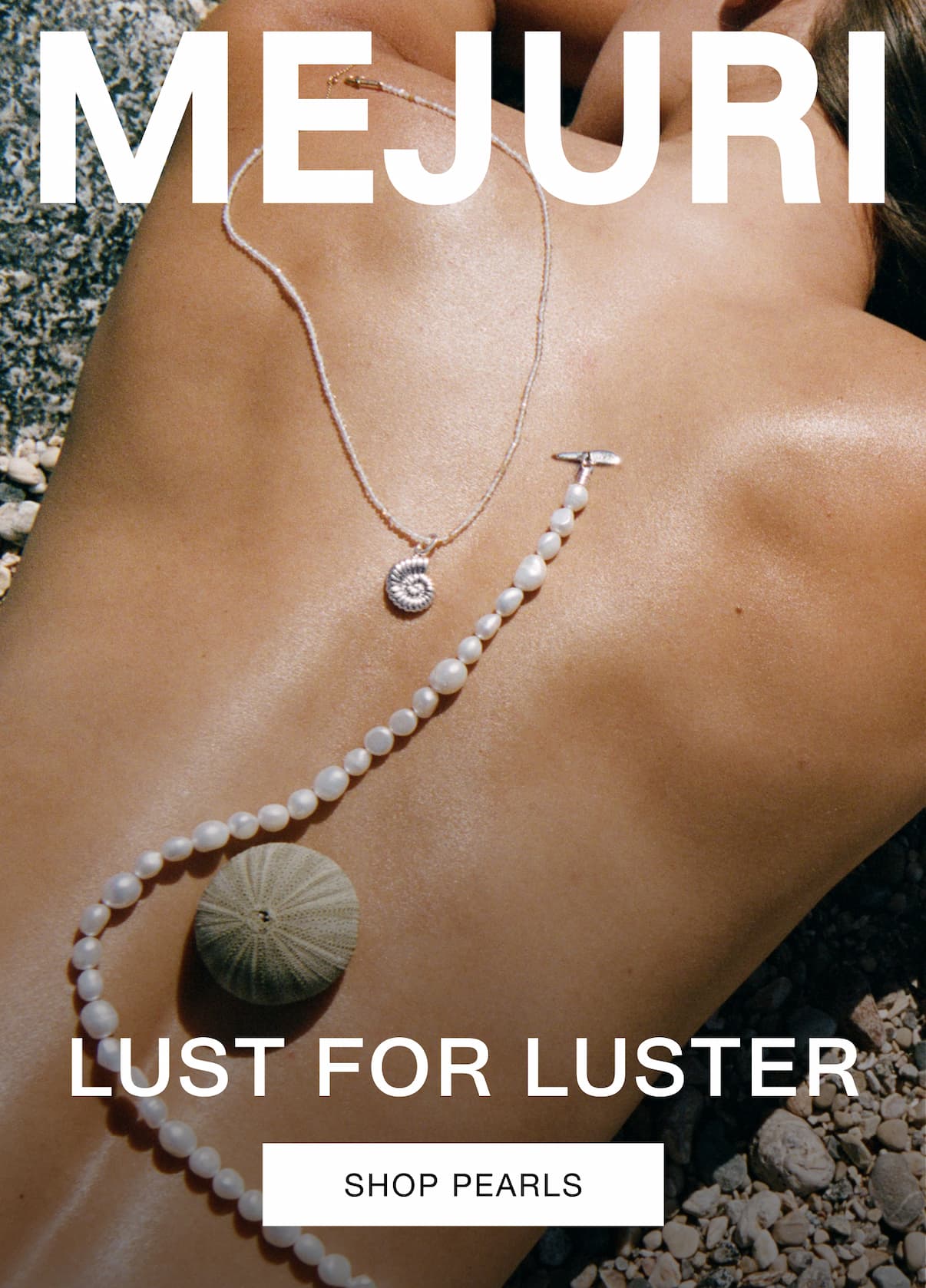 Close-up of a woman's décolletage on a rocky beach styled with a Mejuri pearl strand necklace and a silver shell pendant necklace — Lust for Luster, Shop Pearls.
