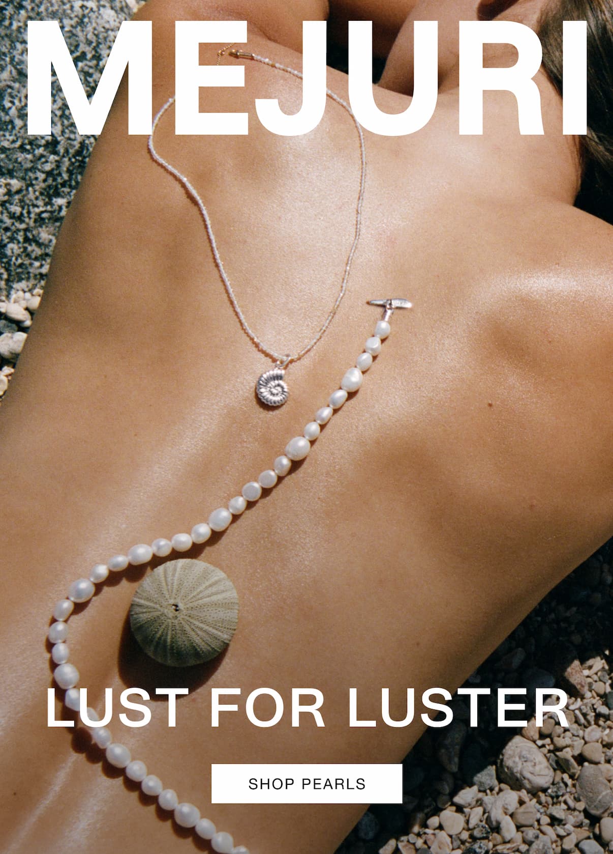 Close-up of a woman's décolletage on a rocky beach styled with a Mejuri pearl strand necklace and a silver shell pendant necklace — Lust for Luster, Shop Pearls.