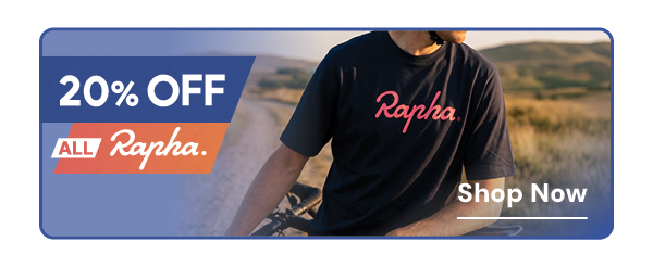 20% OFF ALL RAPHA. A man leans against his bike at the roadside, wearing Rapha Men's Cotton Large Logo T-Shirt in Navy/Pink