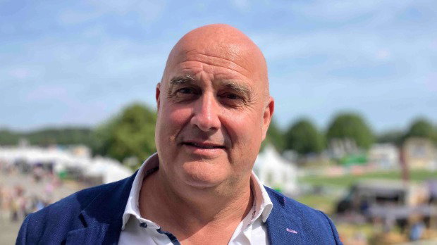 A close-up of Richard Clothier, managing director of Wyke Farms, a middle-aged man wearing a blue jacket and white shirt. He is standing in a large field at the Royal Bath and West Show.’