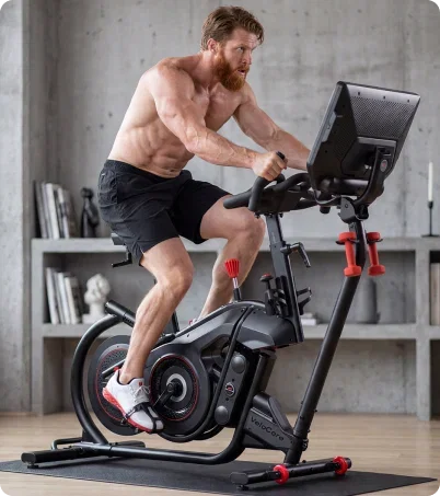 Shirtless man with a beard riding BowFlex VeloCore bike in industrial setting