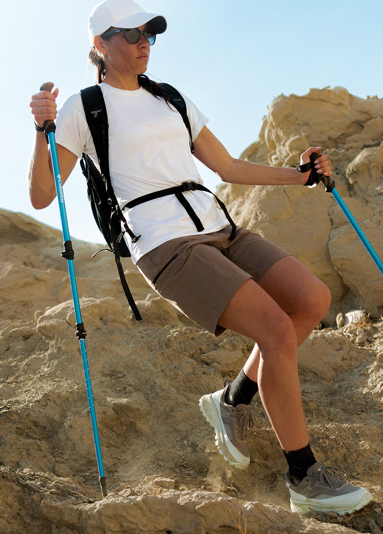 Woman hiking down rocks with trekking poles. 