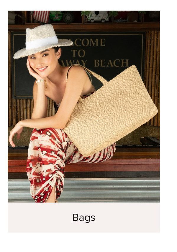 Woman in a hat holding a large woven bag, sitting on a bench.