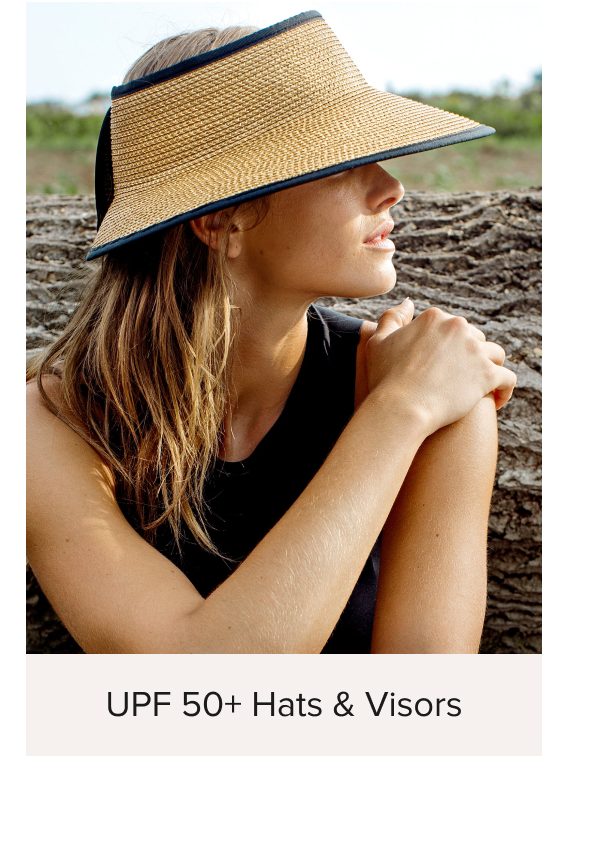 Woman wearing a straw visor hat, sitting outdoors with arms crossed.