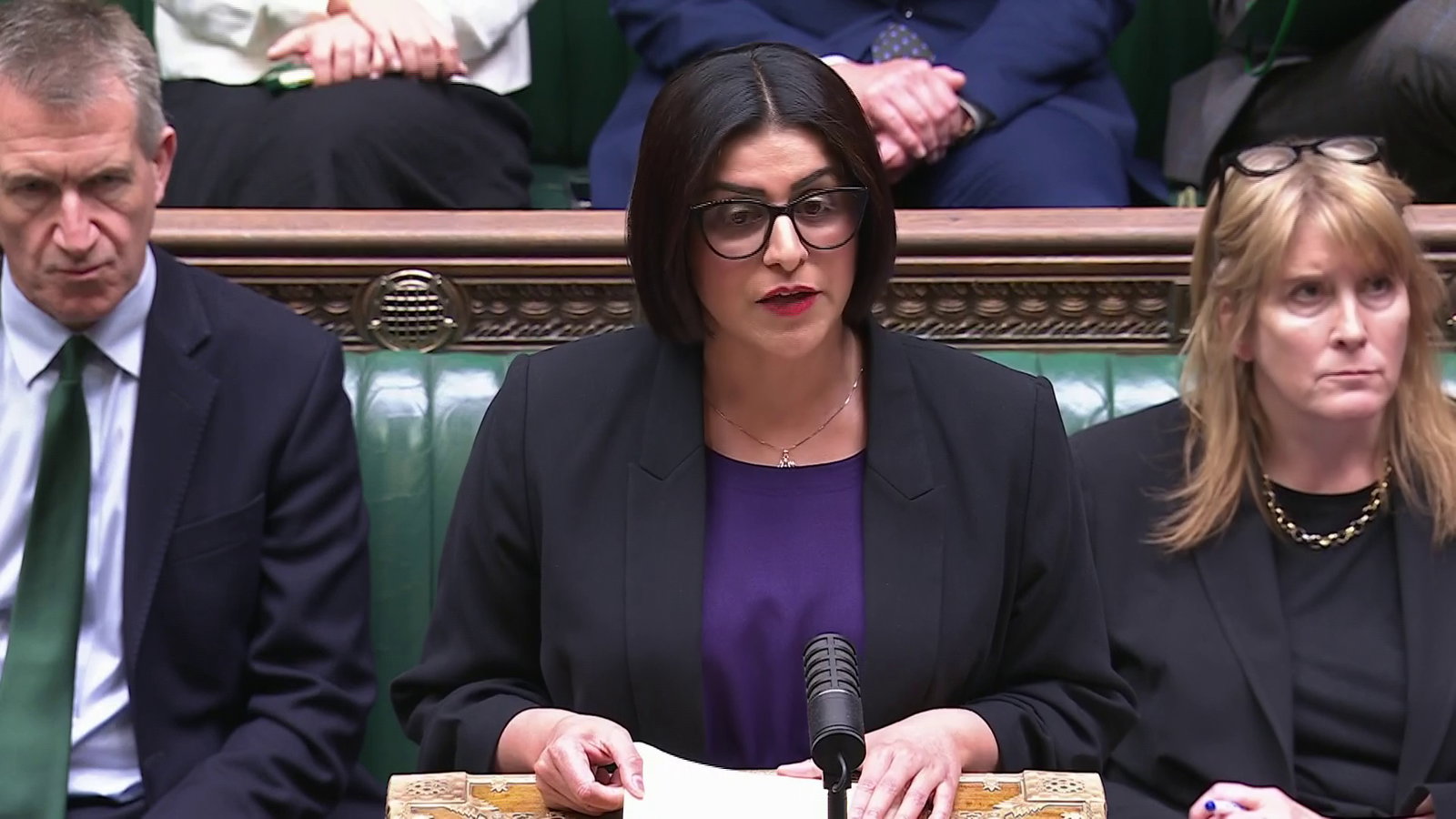 Home Secretary Shabana Mahmood speaking in the Commons with a microphone in front, on a lectern. Mahmood wears glasses and has bob-length dark hair. Behind her MPs are seated on green benches.