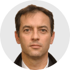 Damian Grammaticas has short dark hair and wears a white shirt and black collared jacket in this headshot.