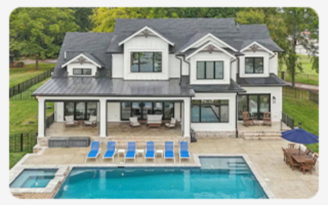 Large lakeside home with covered patio, pool, blue loungers, and outdoor seating overlooking the water.