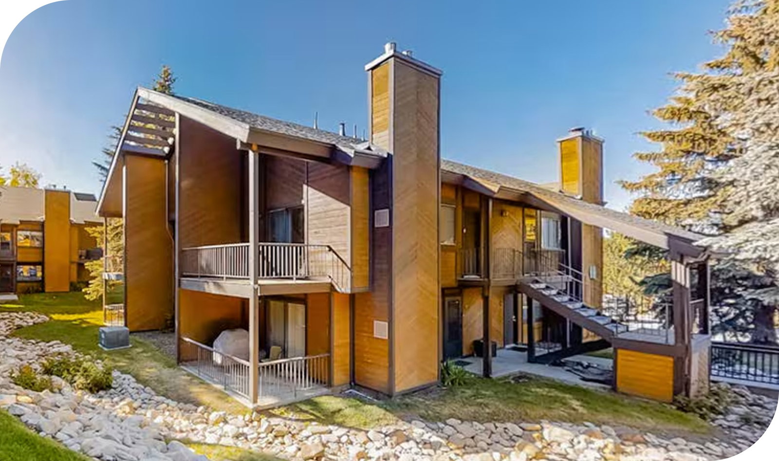 Modern chalet-style building with balconies and exterior staircases set among trees.