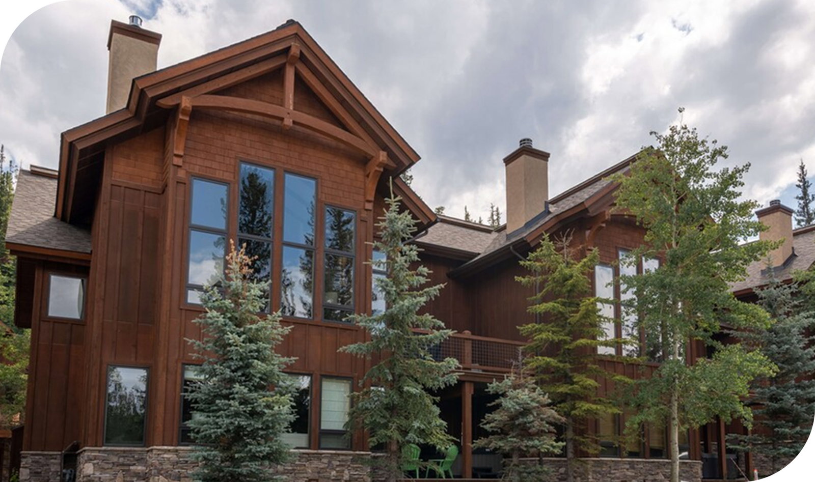 Upscale mountain home with dark wood tone exterior, large windows, and pine trees framing it.