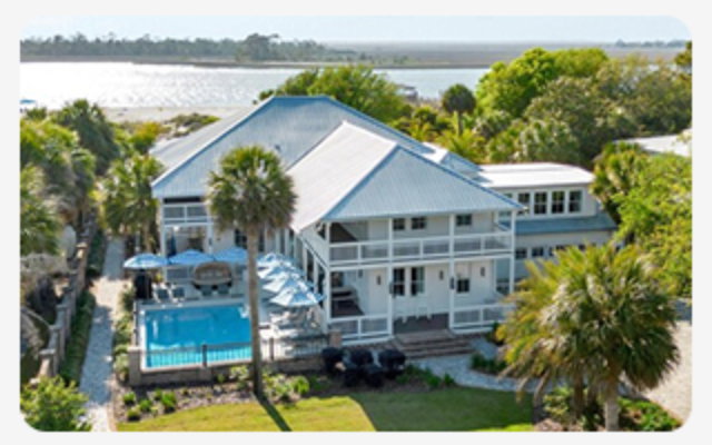 Coastal home with wraparound balconies, palm trees, and a backyard pool near the shoreline.