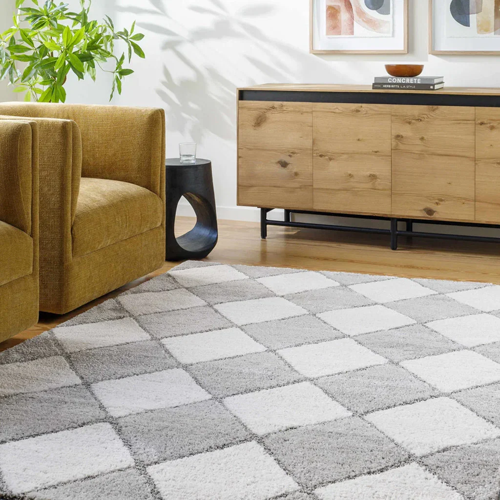 Modern living room with mustard yellow armchair, wooden sideboard, and neutral checkered area rug from Boutique Rugs collection.